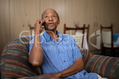 Senior man talking on mobile phone while sitting on sofa