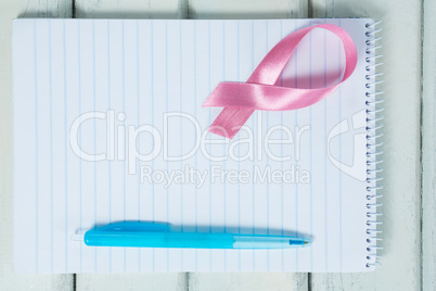 Overhead view of pink Breast Cancer Awareness ribbon and spiral notepad with pen