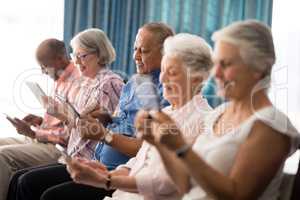 Smiling senior people using digital tablets while sitting on chairs