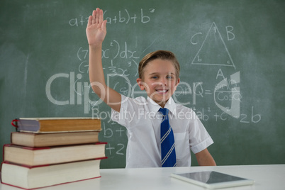 Schoolboy raising hand while sitting in classroom