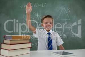 Schoolboy raising hand while sitting in classroom