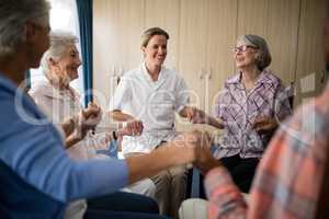 Smiling female doctor holding hands with seniors while sitting on chairs
