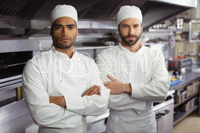 Portrait of two chefs standing together with arms crossed in commercial kitchen