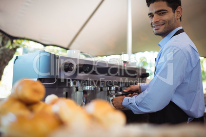 Smiling waiter making cup of coffee from espresso machine