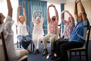 Seniors stretching with female doctor while sitting on chairs