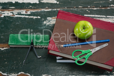 Various stationery with books and apple on wooden table