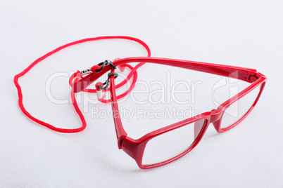 Red reading glasses with a red neck strap on a white surface