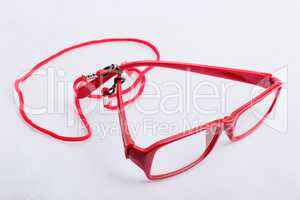 Red reading glasses with a red neck strap on a white surface