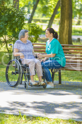 Caregiver talking to disabled senior woman in wheelchair outdoor