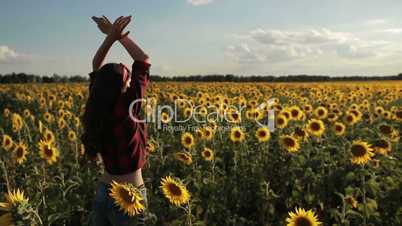 Girl standing with arms raised in sunflower field