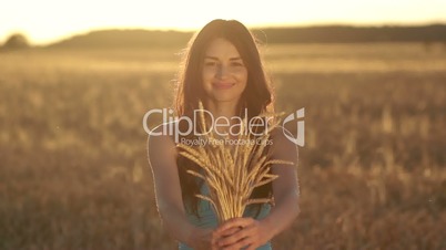 Lovely girl holding ripened wheat ears on field