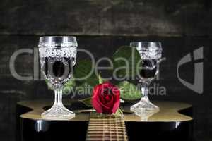 Red Rose and Wine Glasses Resting On Acoustic Guitar With Wooden