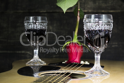 Glass Of Red Wine Resting on Acoustic Guitar With Red Rose and a