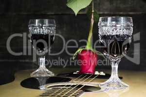 Glass Of Red Wine Resting on Acoustic Guitar With Red Rose and a