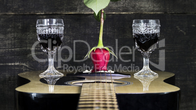 Red Rose and Wine Glasses Resting On Acoustic Guitar With Wooden