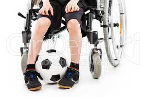 Disabled child boy sitting on wheelchair holding soccer ball