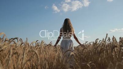 Girl with arms outstretched walking on wheat field