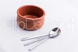 A brown bowl made out of clay and three little spoons