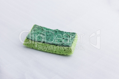 A green used kitchen sponge, with a hard and a soft surface