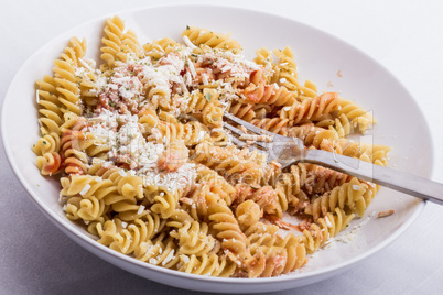 A half full white plate, with fusilli, covered with tomato sauce