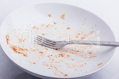 An empty, used white plate, with remains of fusilli, covered wit