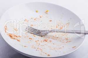 An empty, used white plate, with remains of fusilli, covered wit
