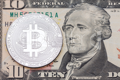 Silver bitcoin coin on ten dollars banknote close up.