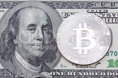 SIlver bitcoin on one hundred dollars banknote.