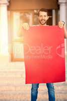 Composite image of portrait of happy man holding red blank cardboard
