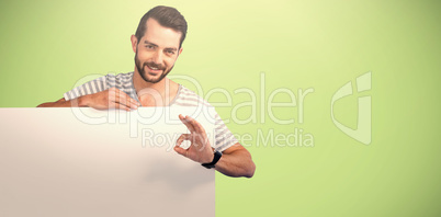 Composite image of portrait of man showing ok sign while holding blank cardboard