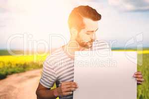 Composite image of young man looking at blank cardboard