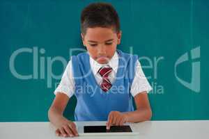 Composite image of schoolboy using digital tablet at table