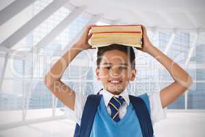 Composite image of smiling schoolboy carrying books on head over white background