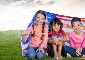 Kids sitting under american flags in field