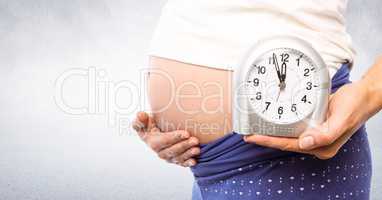 Pregnant woman holding clock with bright background