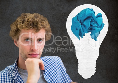 Man standing next to light bulb with crumpled paper ball in front of blackboard