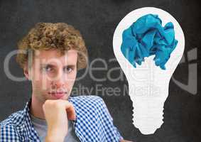 Man standing next to light bulb with crumpled paper ball in front of blackboard