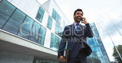 Excited business man talking on the phone against building background