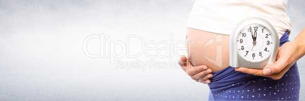 Pregnant woman holding clock in front of grey background