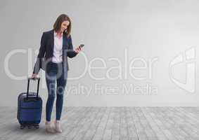 Happy business woman using a phone and holding a suitcase against white wall background