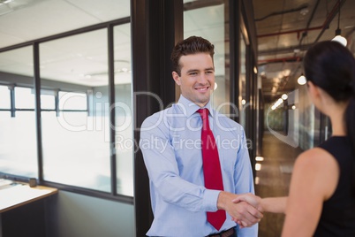 Happy business people shaking hands against office background