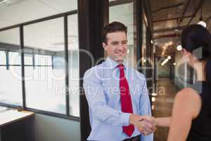 Happy business people shaking hands against office background