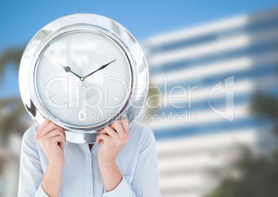 Woman holding clock in front of city buildings