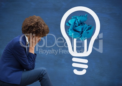 Woman sitting next to light bulb with crumpled paper ball in front of blackboard