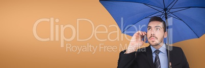 Business man with blue umbrella talking on the phone against orange background