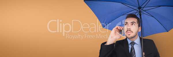 Business man with blue umbrella talking on the phone against orange background