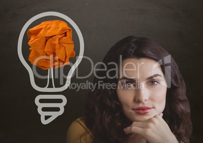 Woman standing next to light bulb with crumpled paper ball in front of blackboard