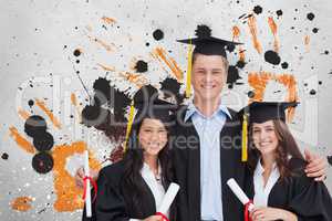 Happy young students holding diplomas against grey, yellow and black splattered background