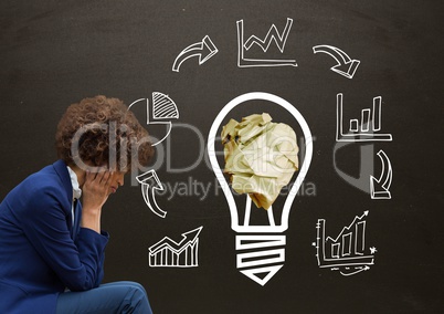 Woman sitting next to light bulb with crumpled paper ball and business graphics in front of blackboa