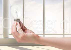 Hand holding light bulb in front of window